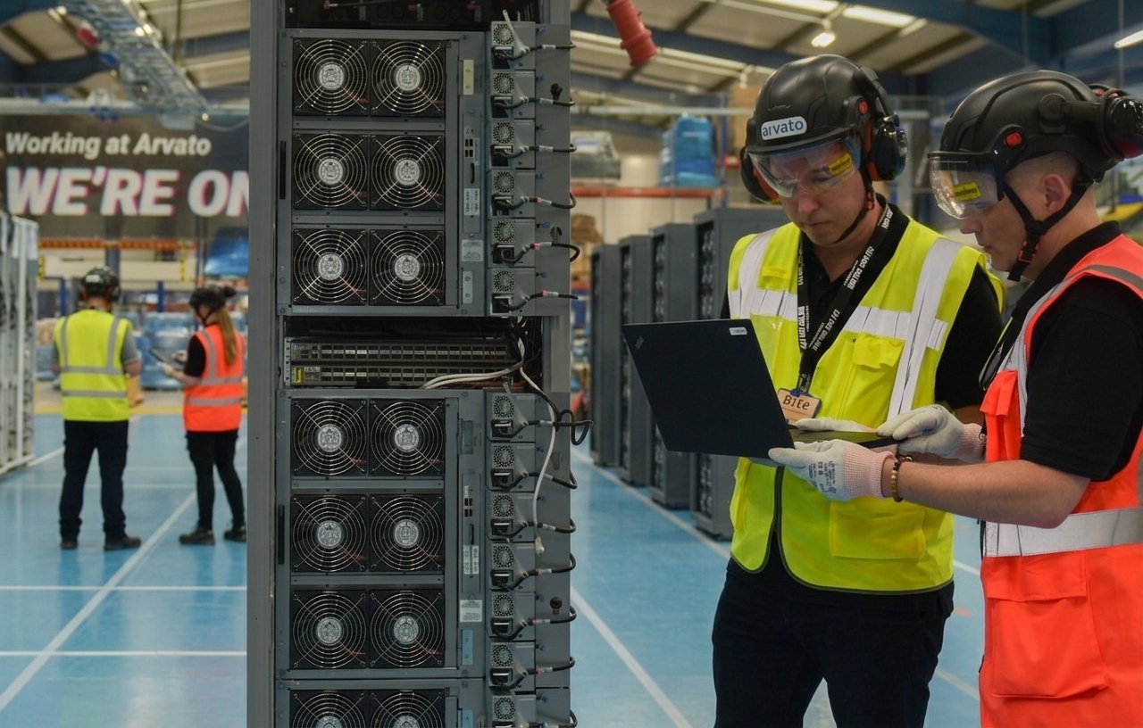 Two Arvato technicians checking a laptop beside a fan-wall rack