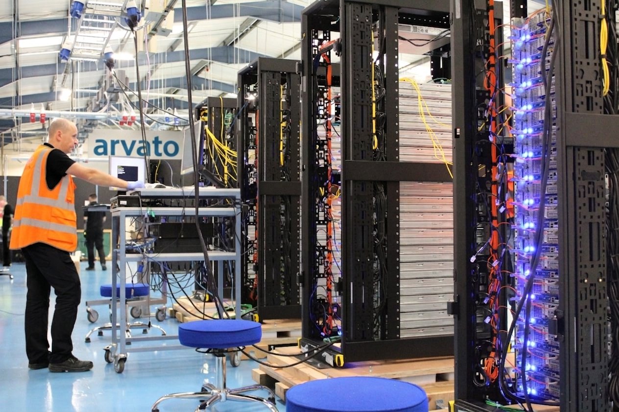 A technician at a laptop beside populated server racks on the integration floor